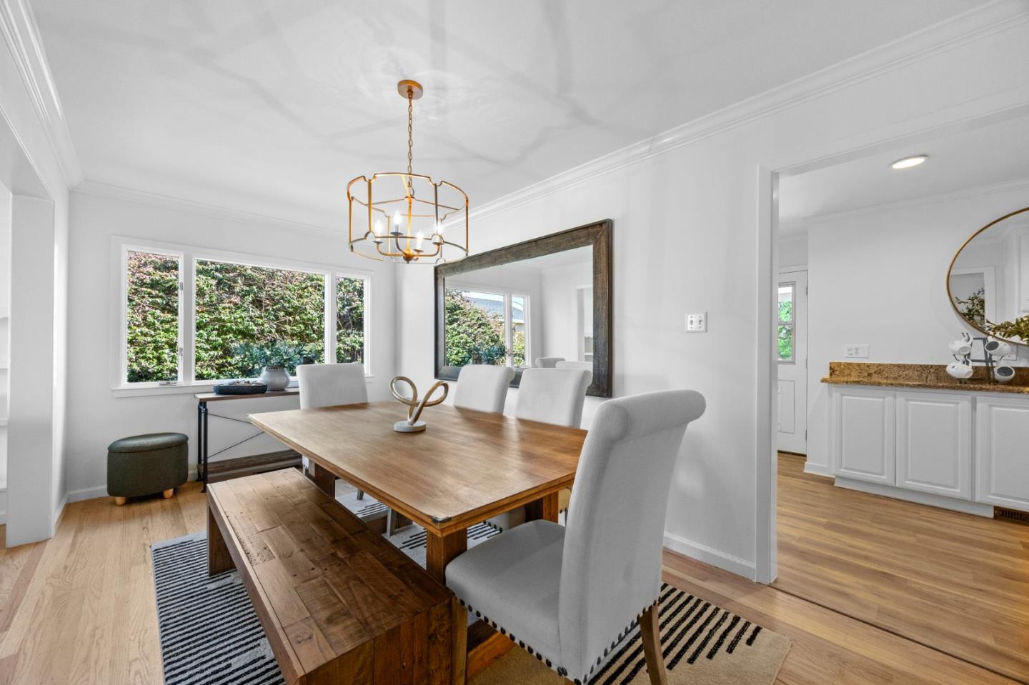 Dining room with a long wood table, bench, upholstered chairs, and large windows overlooking greenery.