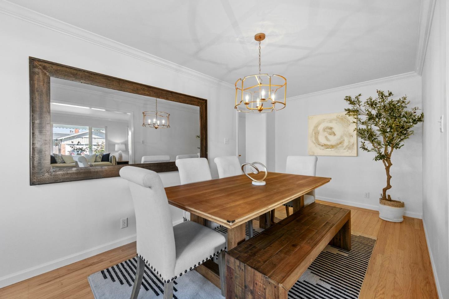Dining room with a wooden table and bench, white chairs, and a large framed mirror.