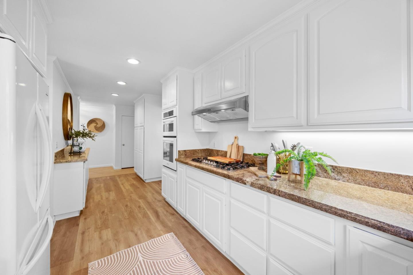 Kitchen with white cabinets, granite countertops, a gas cooktop, and warm wood flooring.