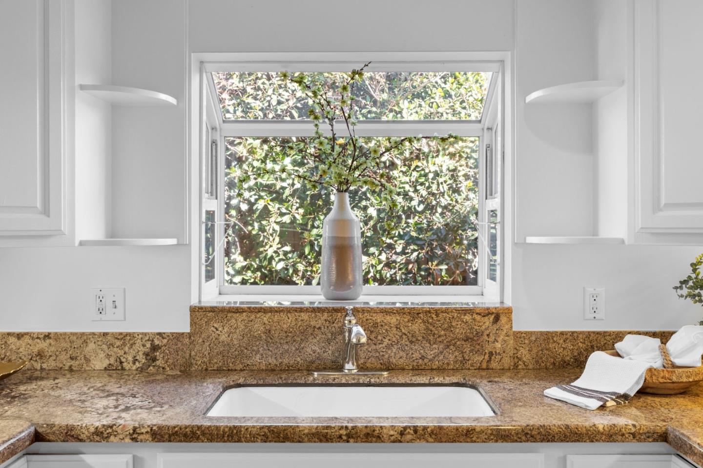Bathroom vanity with a granite counter, white sink, and a window framing leafy greenery.