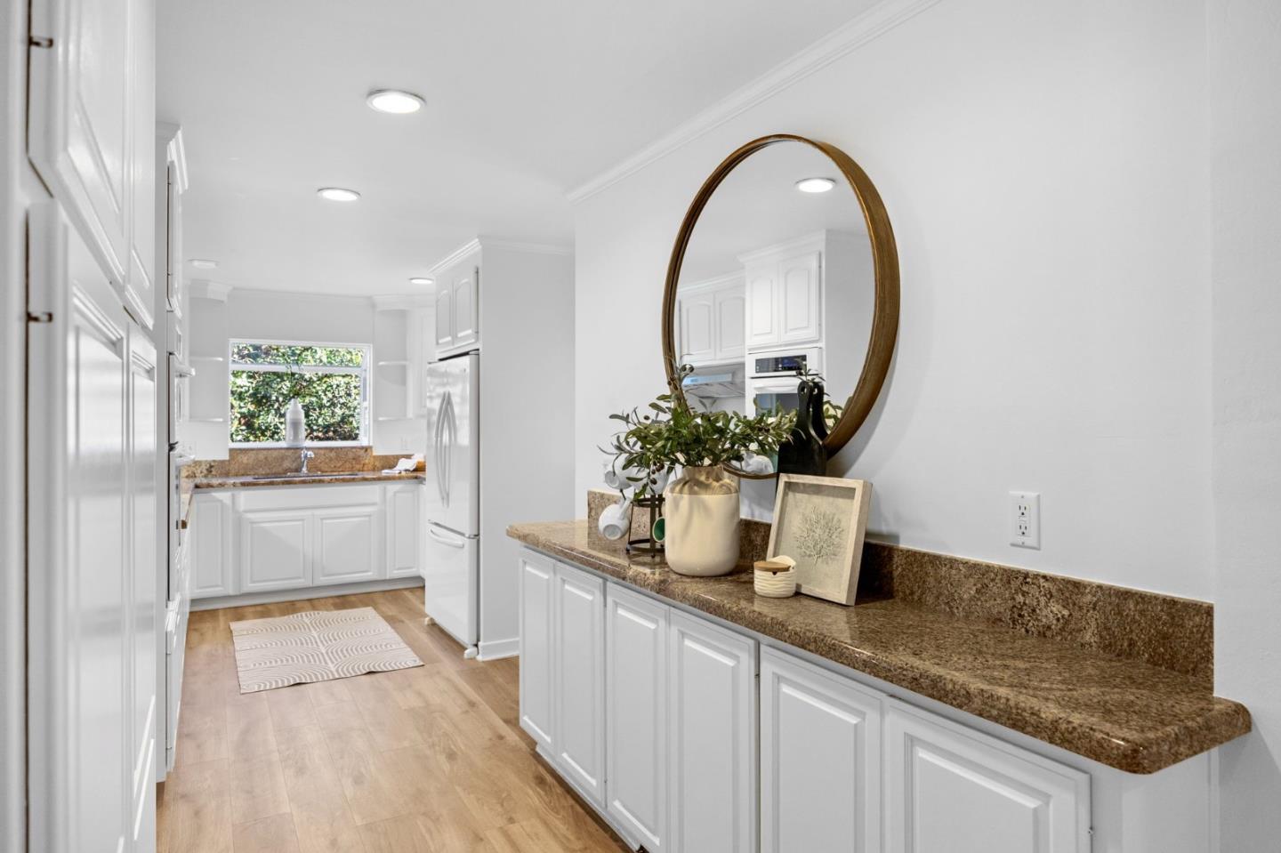 Bright white kitchen with granite counters, stainless appliances, and a round mirror above the foreground counter.