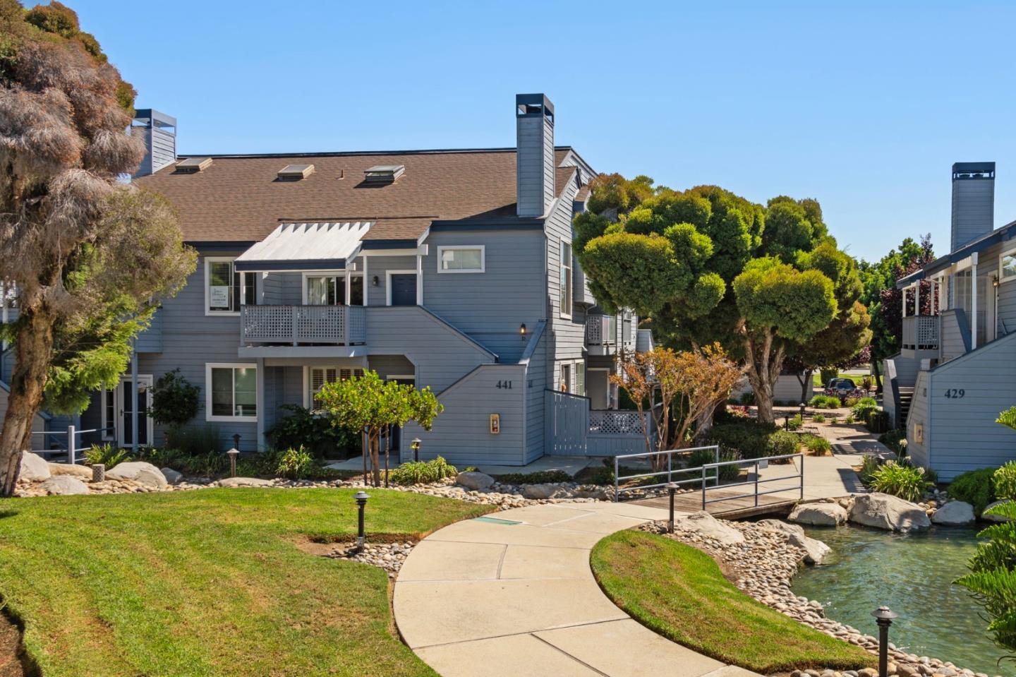 Blue-gray residential building at 441 with balconies, a landscaped lawn, and a walkway beside a small waterway.