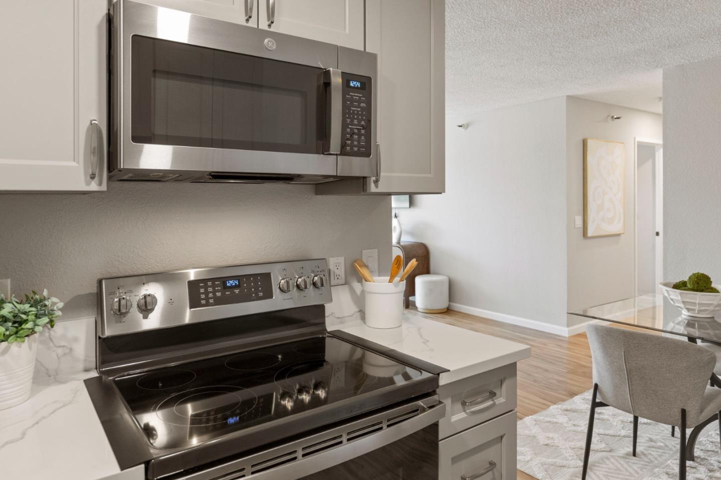 Condo kitchen with white cabinetry, stainless steel appliances, and a black glass cooktop opening to a dining area.