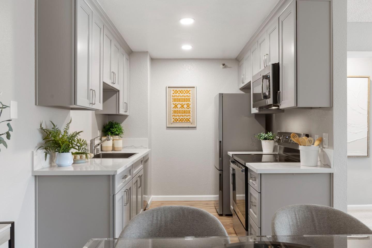 Galley kitchen with gray cabinets, white counters, stainless-steel appliances, and yellow geometric artwork.