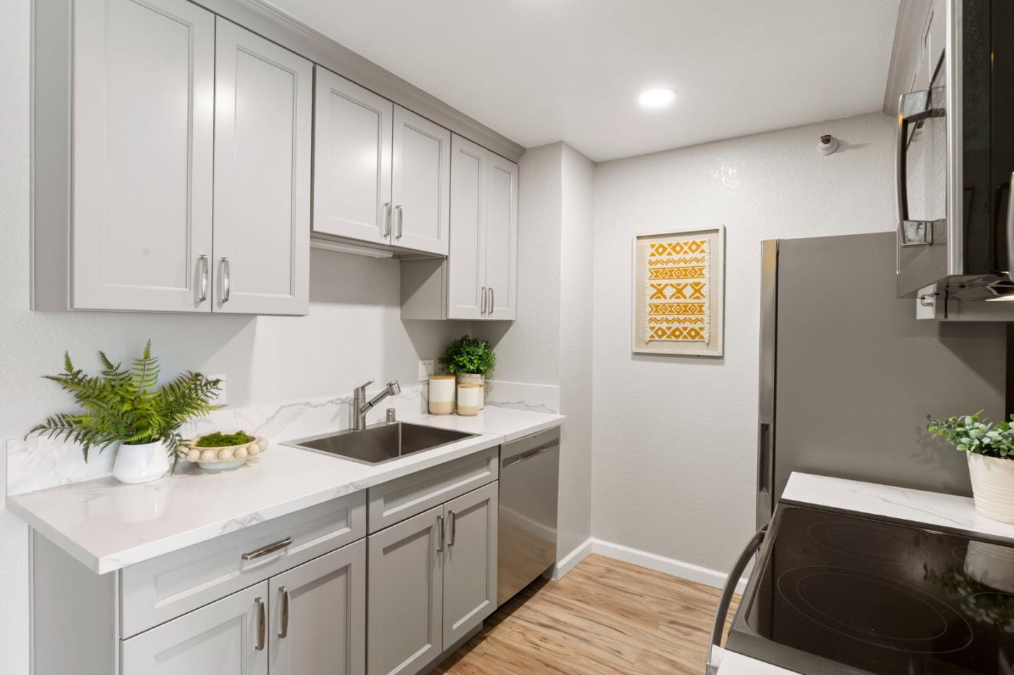 Staged kitchen with white cabinets, marble-look counters, stainless appliances, and light wood flooring.