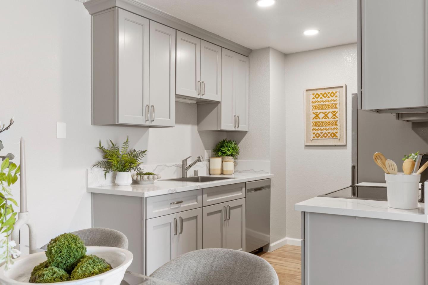 Staged kitchen with gray shaker cabinets, marble-look counters, an island cooktop, and framed geometric artwork.