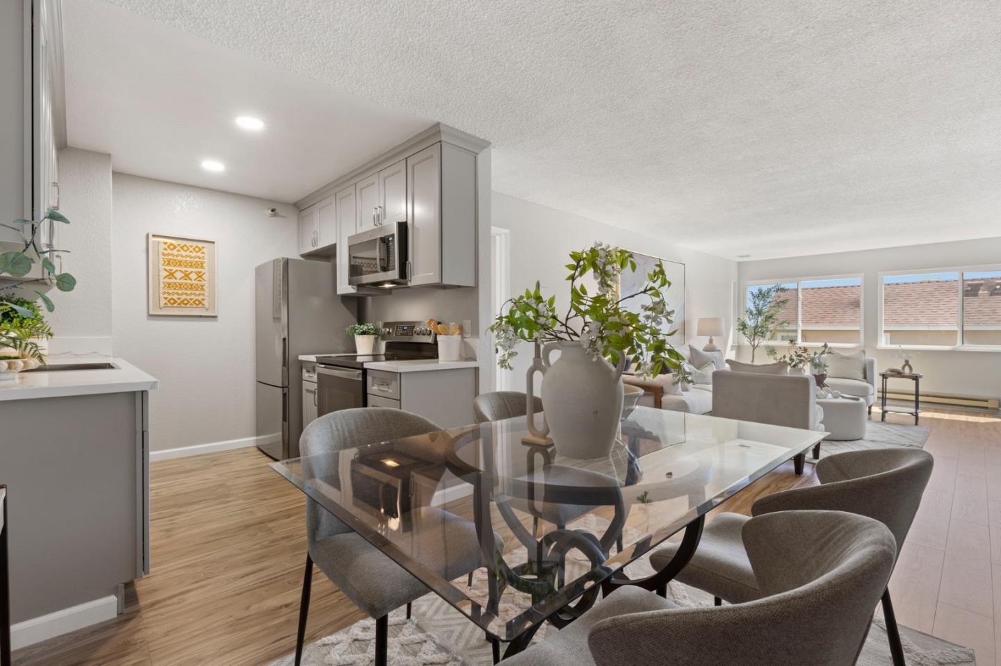 Open-plan condo kitchen and dining area with gray cabinets, a glass table, and bright living room windows.
