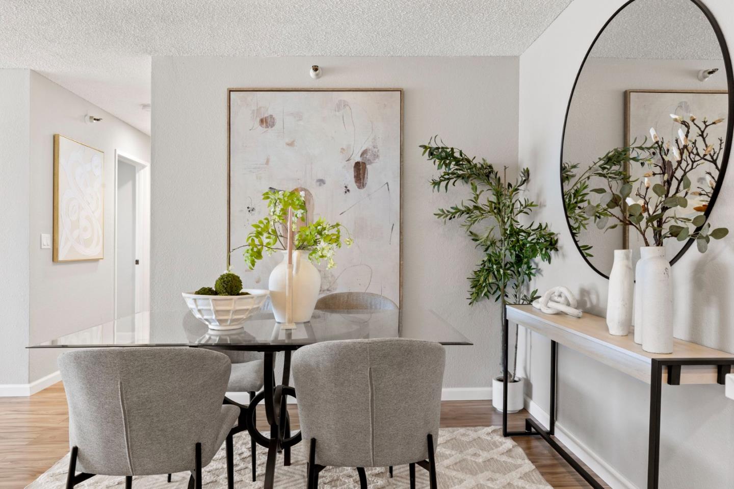 Dining area with a glass-top table, upholstered chairs, abstract art, and a large oval mirror.