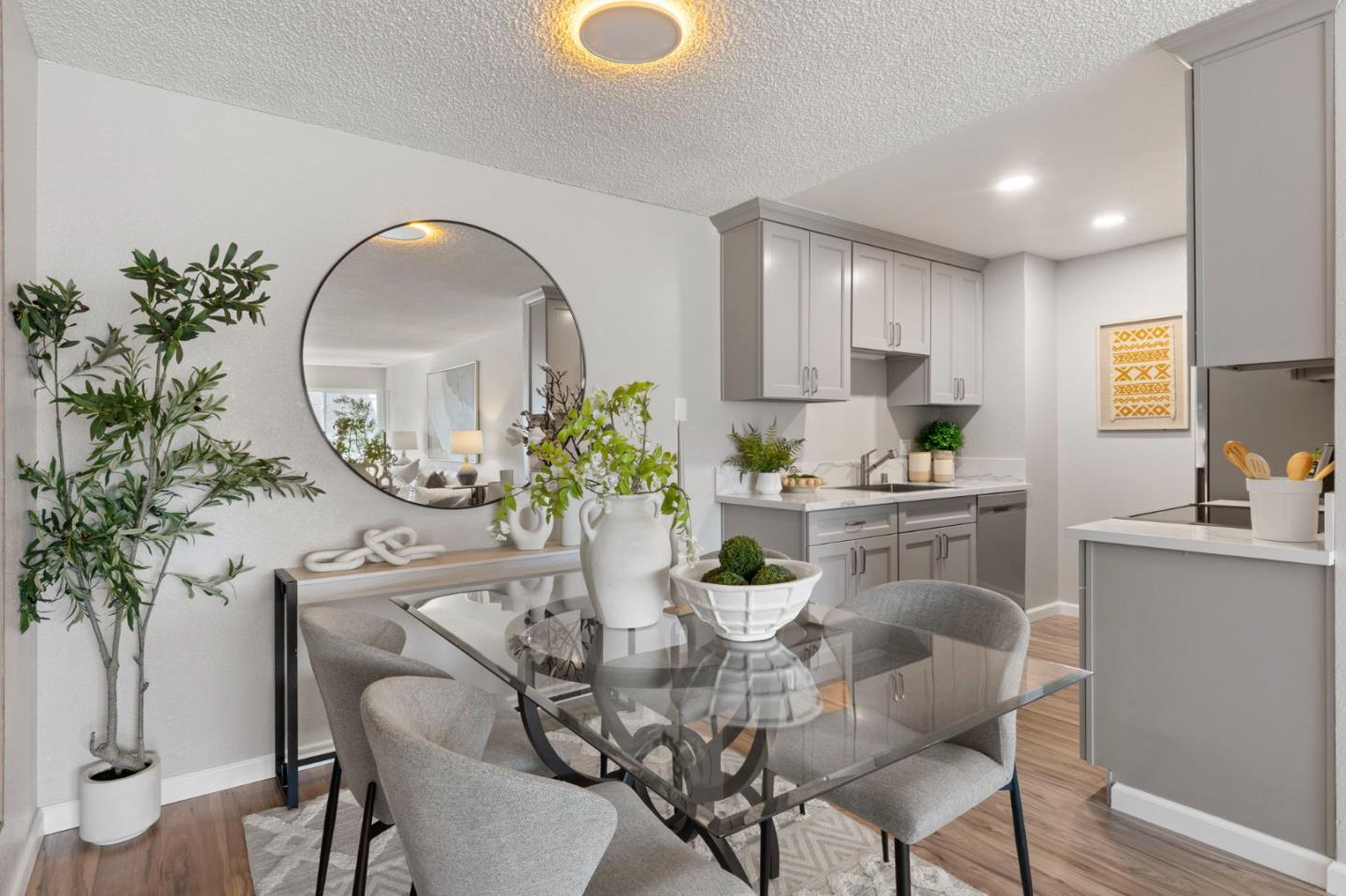 Dining area with a glass table and upholstered chairs beside a gray-cabinet kitchen.