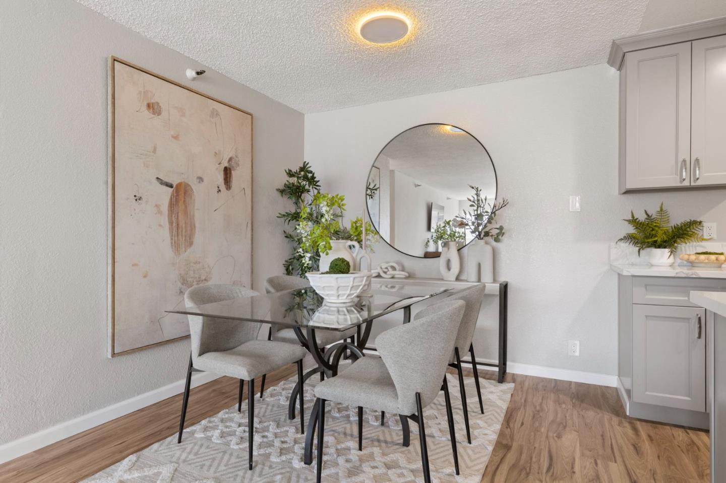 Dining area with a glass-top table, upholstered chairs, large abstract artwork, and round mirror.