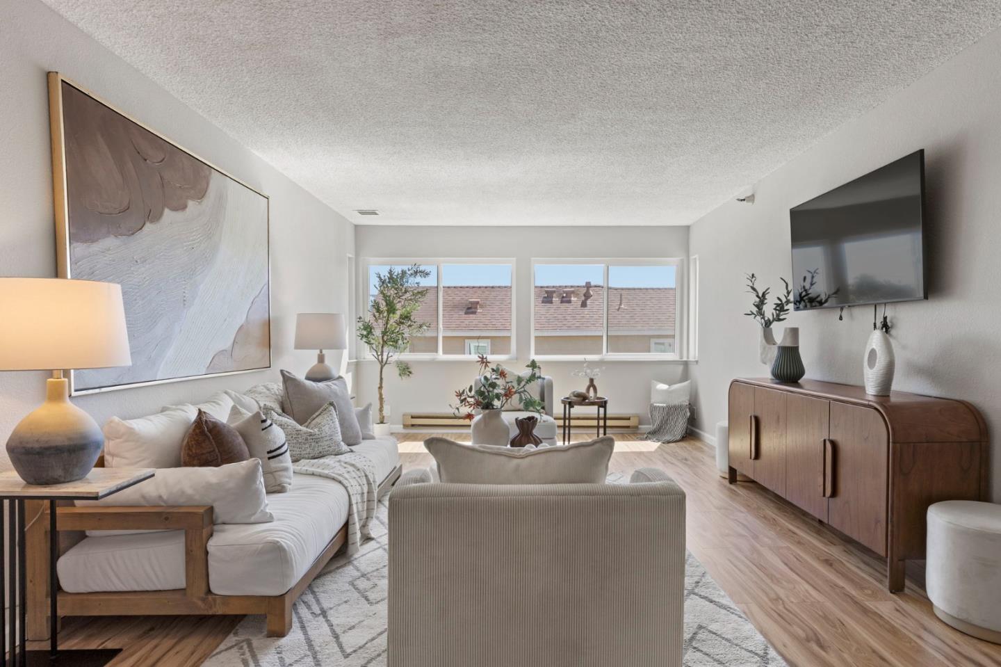 Bright living room with a white sectional, large windows, and a wood media cabinet.