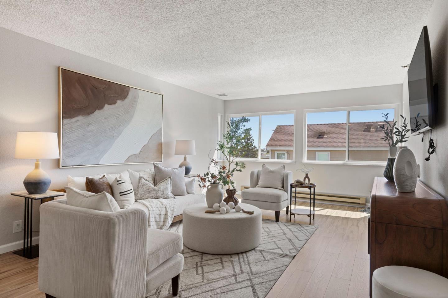 Staged living room with a white sectional, round coffee table, and large windows overlooking rooftops.