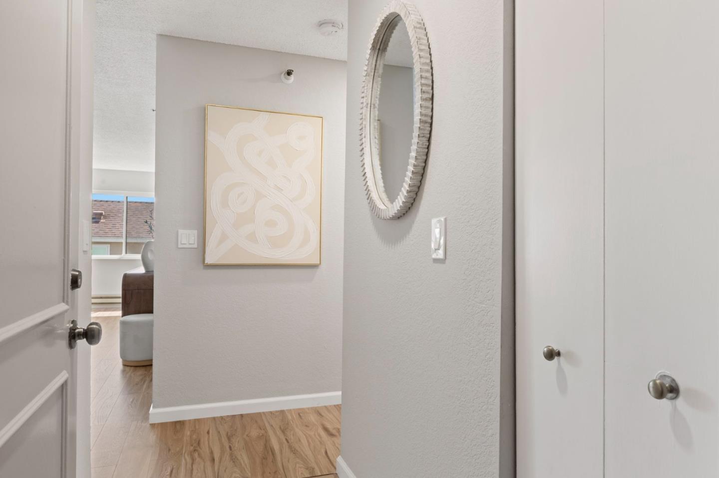 Apartment entry hallway with an oval mirror, white closets, and light wood flooring.