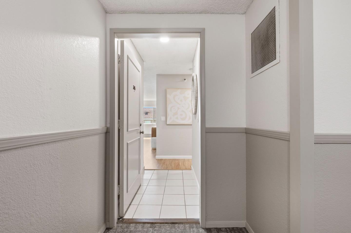 Hallway with carpet and gray wainscoting opens onto a tiled entry and brighter living space.
