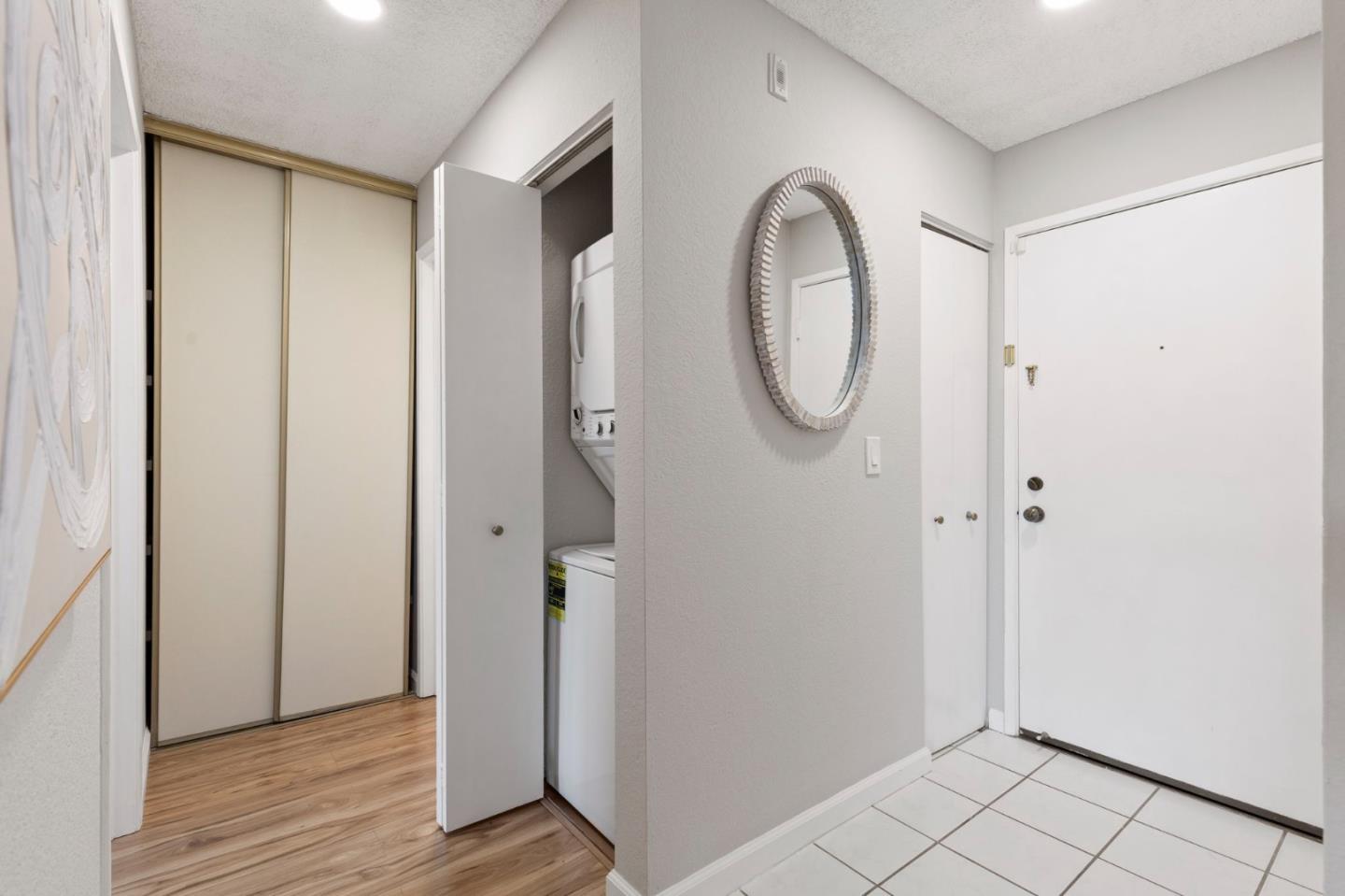 Apartment entryway with a round mirror, tiled floor, sliding closet, and laundry closet.