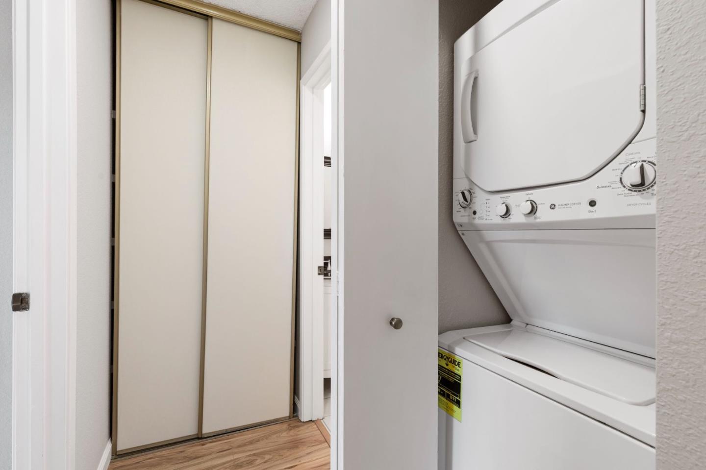 Laundry closet with a stacked washer and dryer beside sliding-door storage.