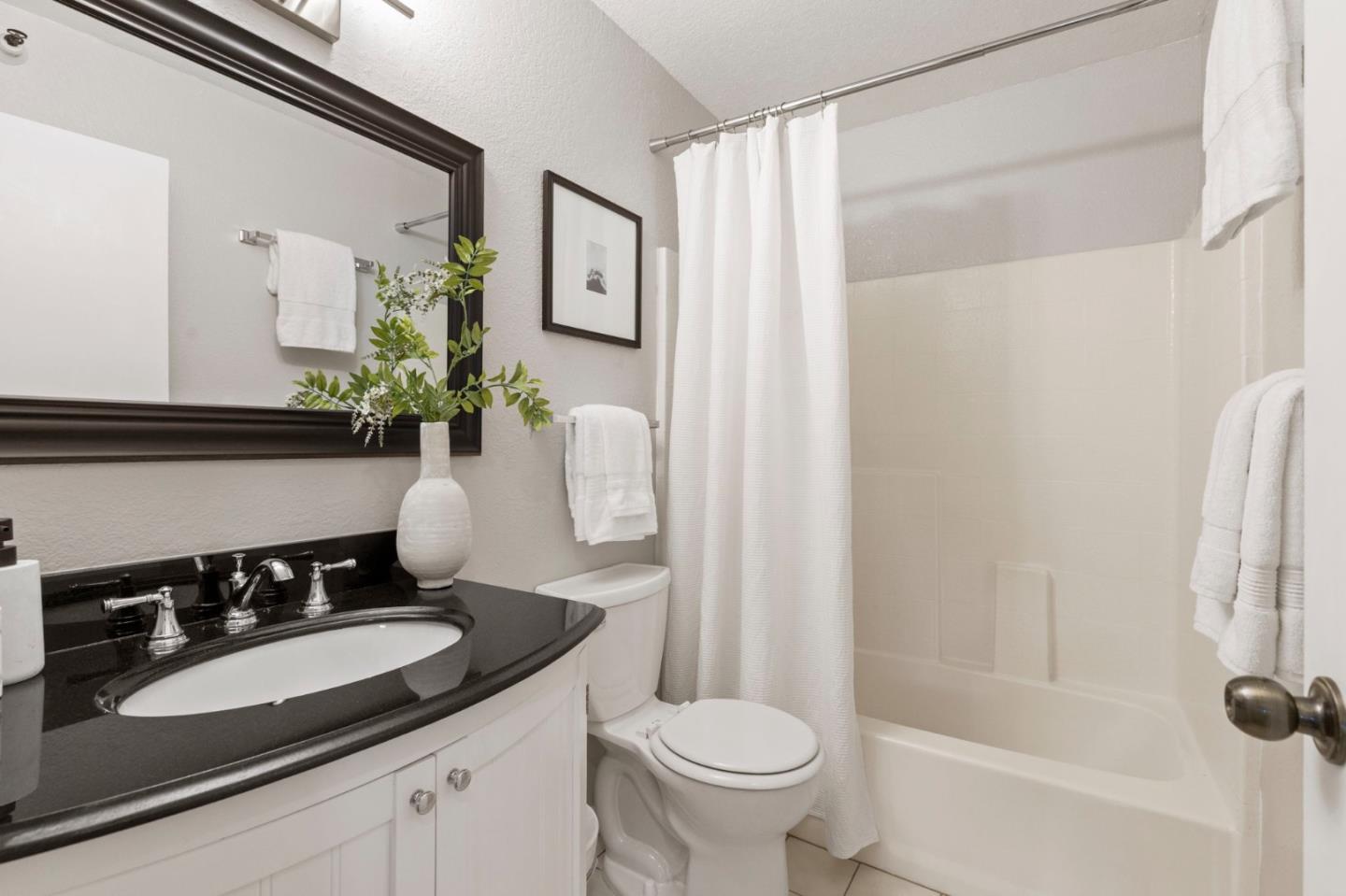 Bathroom with a black countertop vanity, white fixtures, and a tub behind a shower curtain.