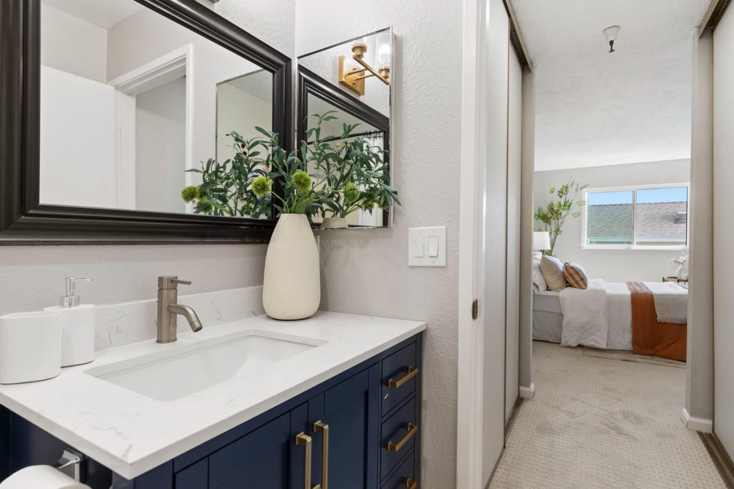 Bathroom with a navy vanity and white countertop, looking through the doorway into a furnished bedroom.