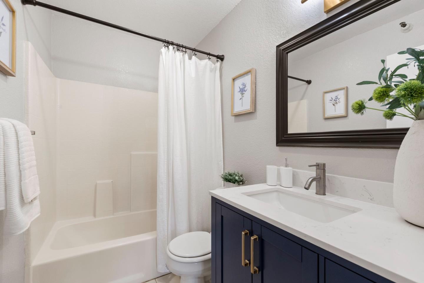 Bathroom with a white tub and shower, navy vanity, and large dark-framed mirror.
