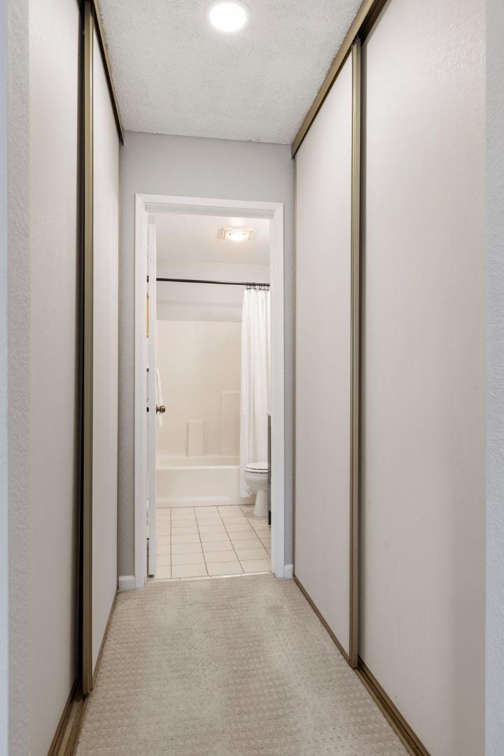 Carpeted hallway with mirrored closet doors leading to a tiled bathroom with a white tub.