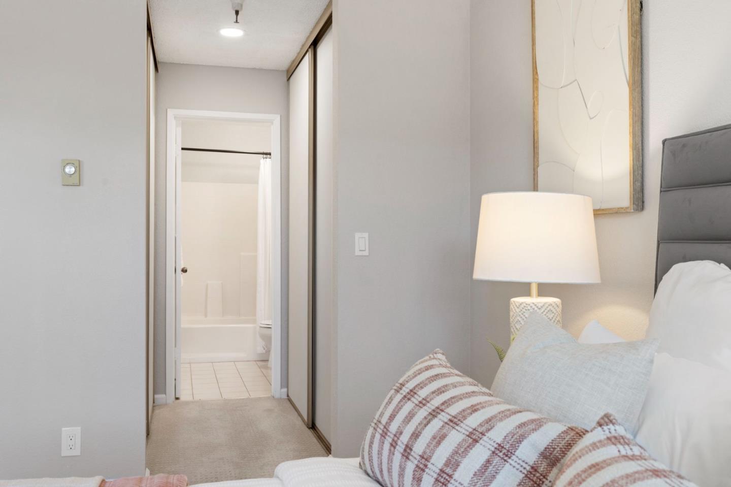 Bedroom with patterned pillows, mirrored closet doors, and an open doorway to the bathroom.