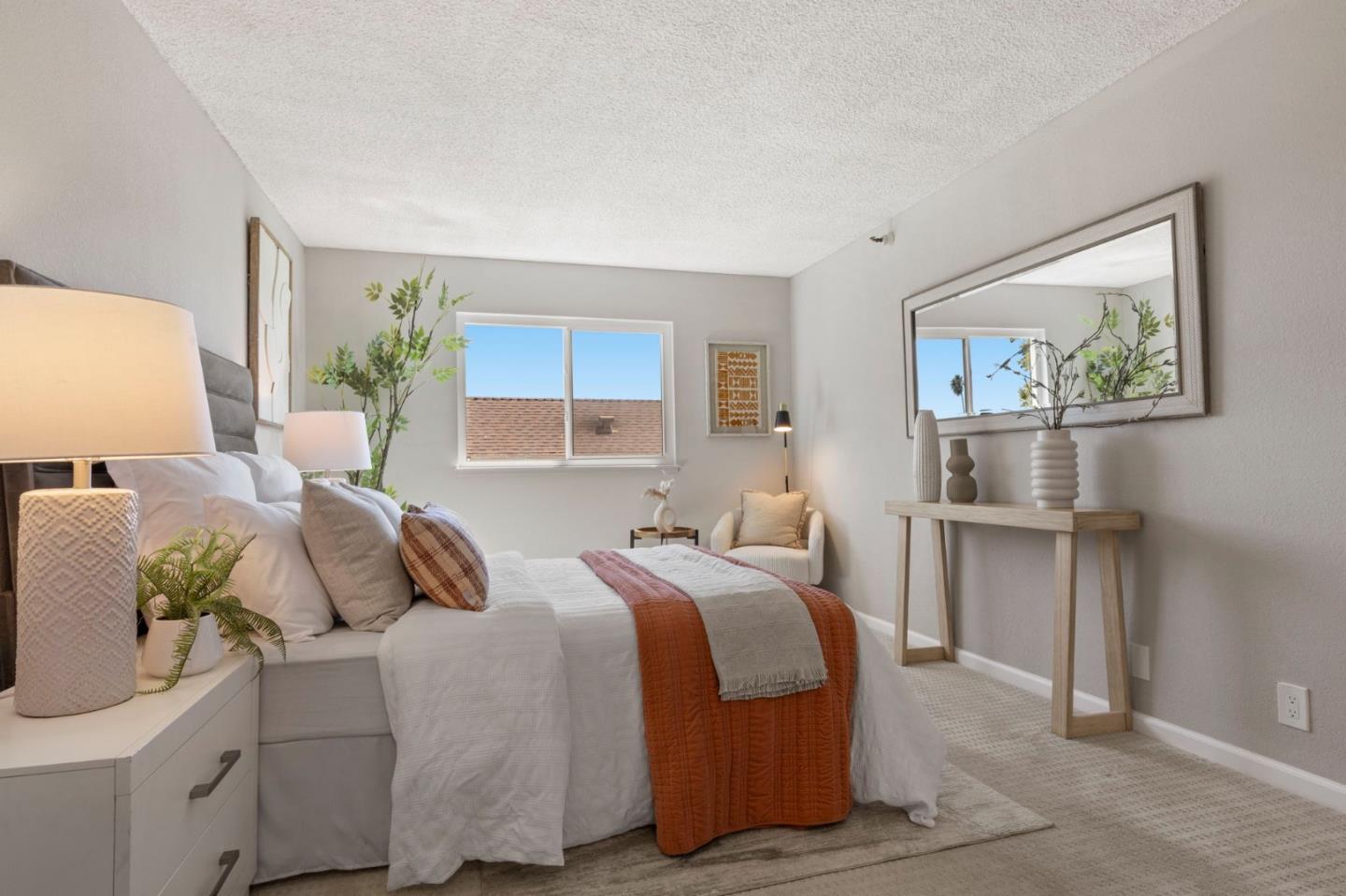 Staged bedroom with white bedding, rust-colored throws, and a large wall mirror.