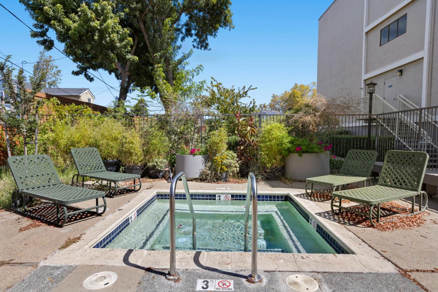 Small outdoor pool with a metal ladder, green lounge chairs, and landscaped planters.