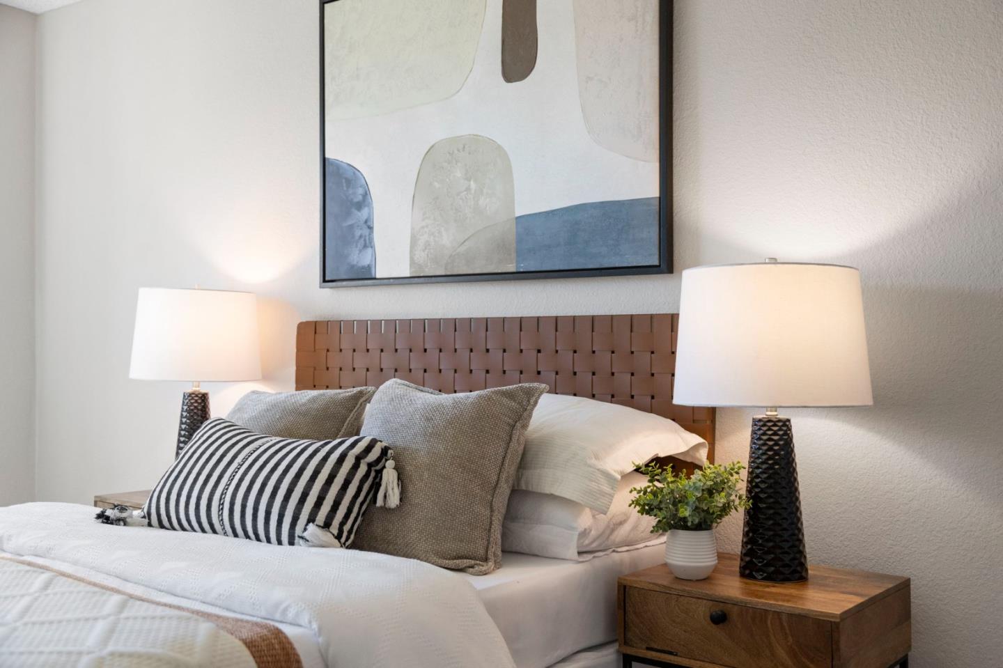 Staged bedroom with a woven headboard, striped pillow, matching lamps, and abstract artwork.