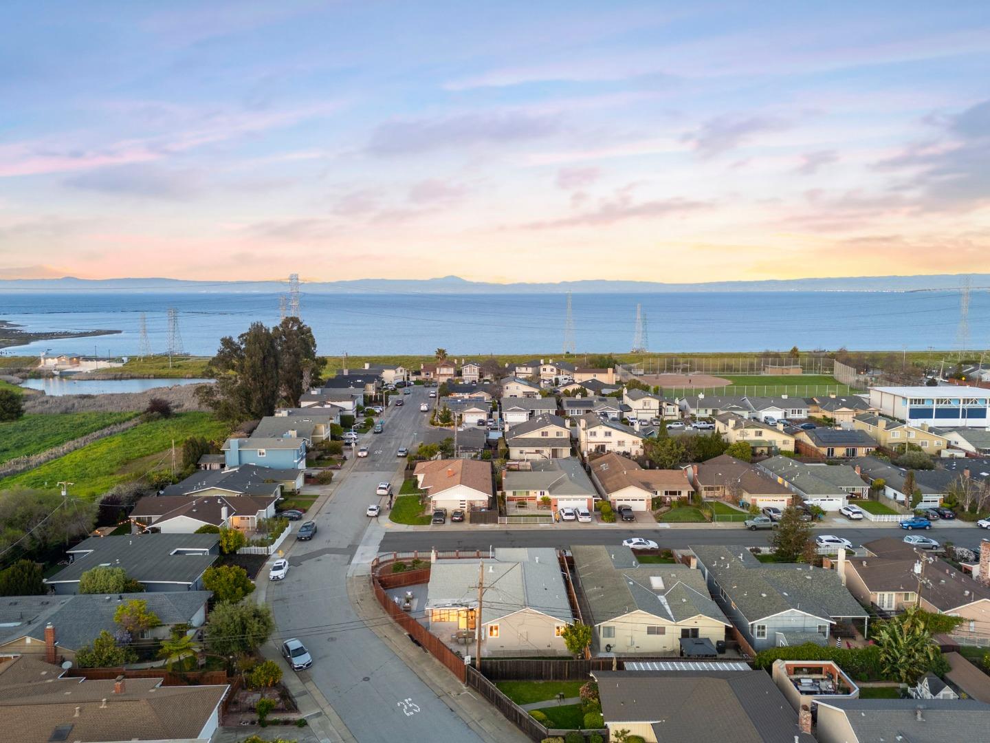 Aerial view of a neighborhood beside the bay, with distant hills under a pastel sunset sky.