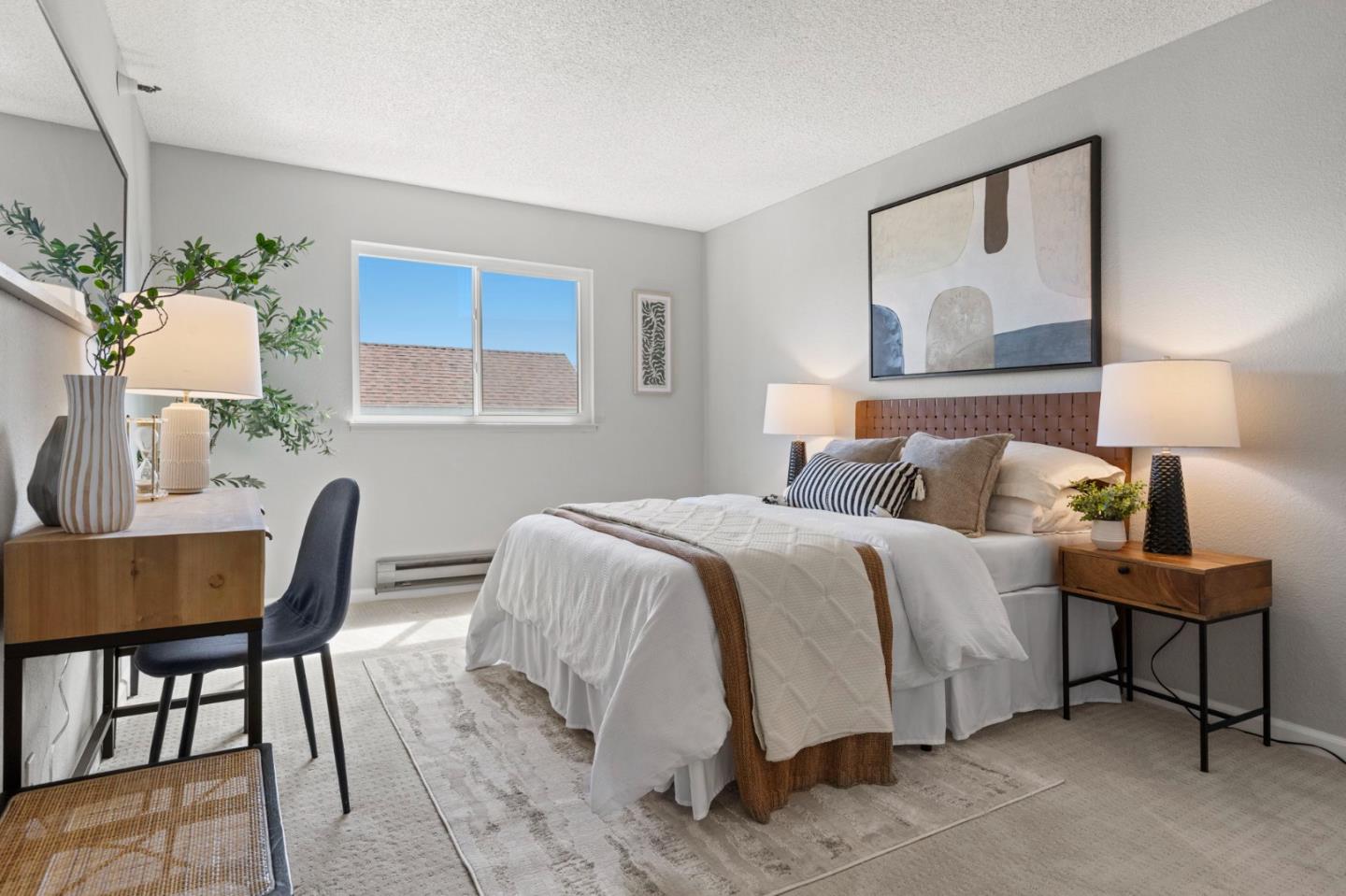 Staged bedroom with a white bed, wood headboard, and desk beside a sunny window.