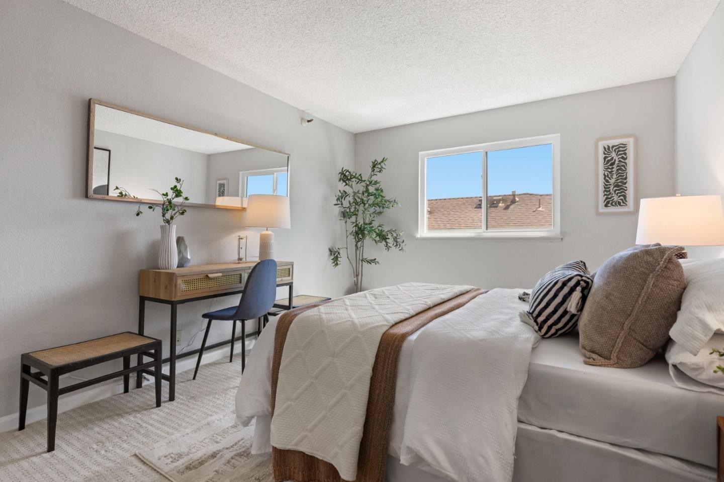 Staged bedroom with a white quilted bed, a desk and blue chair, and a large wall mirror.