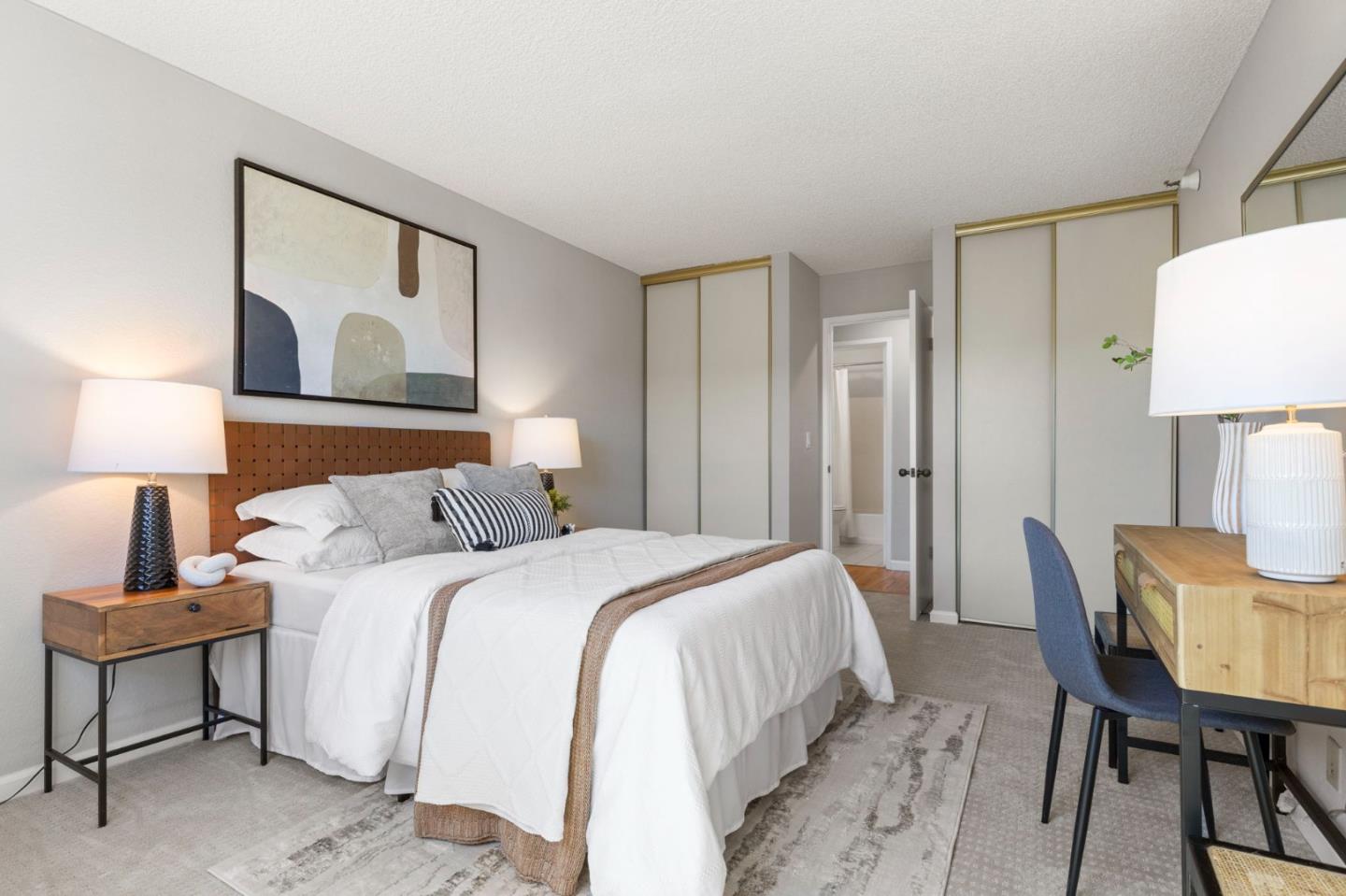 Staged bedroom with a white bed, wooden headboard, and mirrored closet doors.