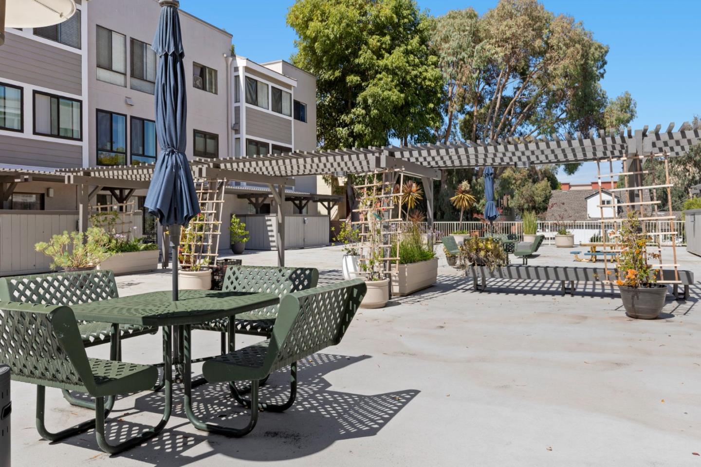 Apartment courtyard with green patio furniture, a slatted pergola, and raised planters.