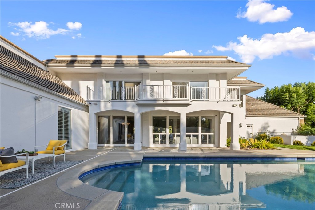 Two-story white home with a balcony overlooking a curved swimming pool and patio seating.