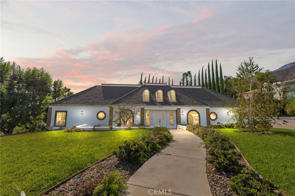 White single-story home with dark tiled roof, arched windows, and landscaped front lawn at sunset.