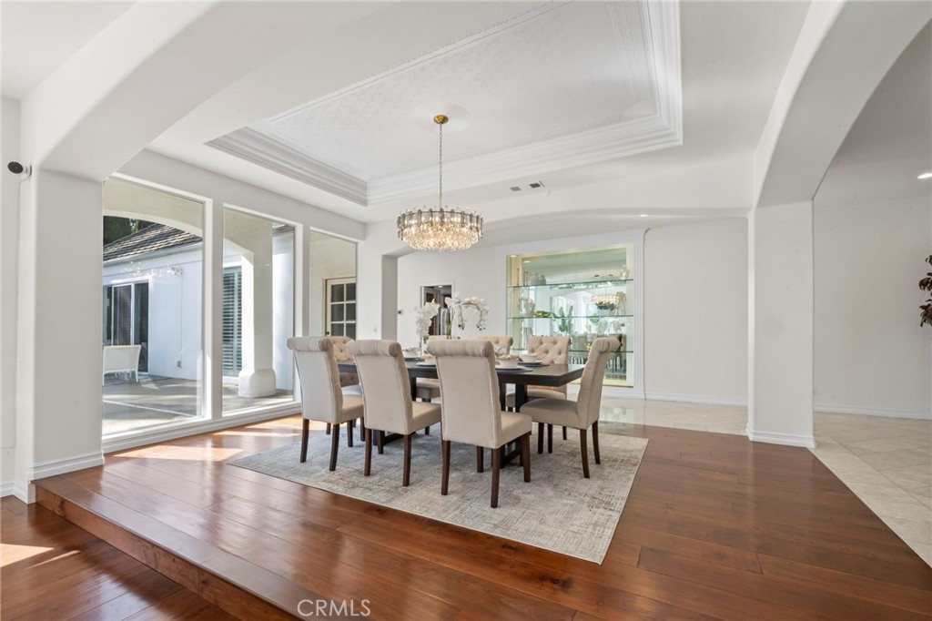 Staged dining room with a crystal chandelier, tray ceiling, and sliding glass doors to a patio.