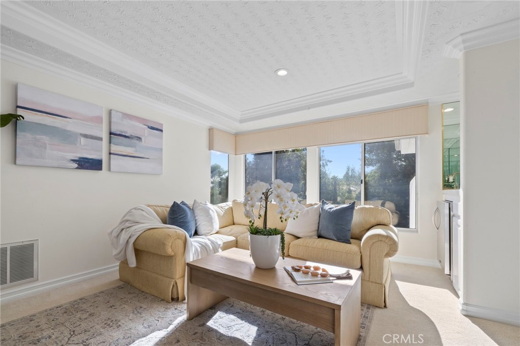 Staged living room with a beige sectional, wooden coffee table, orchids, and large windows.