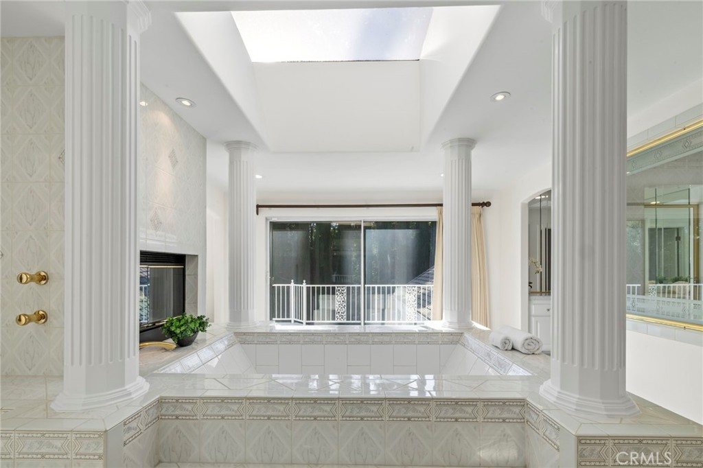 Sunken tiled soaking tub framed by white columns, with a skylight and fireplace.