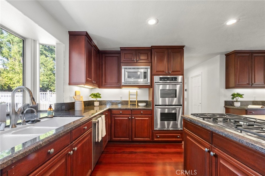Kitchen with rich wood cabinetry, granite counters, a central gas cooktop, and stainless steel double ovens.