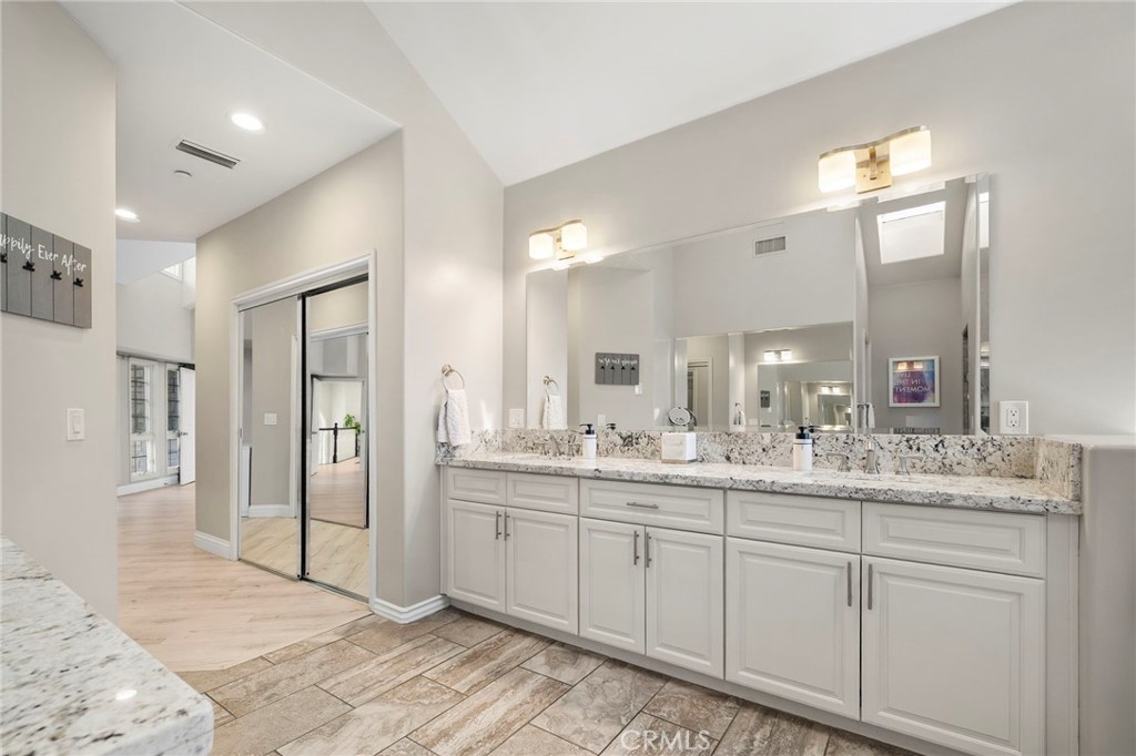 Bathroom vanity with a long stone countertop, large mirrors, and stone-look tile flooring.