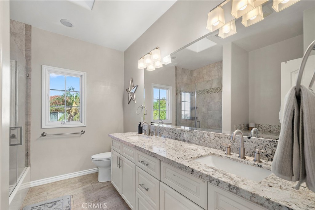 Bathroom with a granite double vanity, large mirror, and tiled glass shower.
