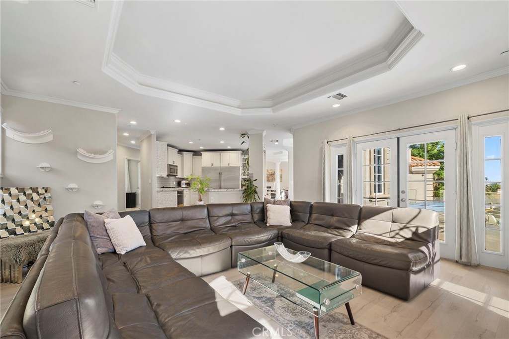 Living room with a brown leather sectional, glass coffee table, and French doors to the patio.