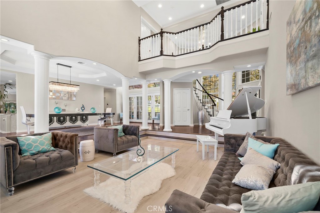 Double-height living room with tufted sofas, a white grand piano, and a curved upstairs balcony.