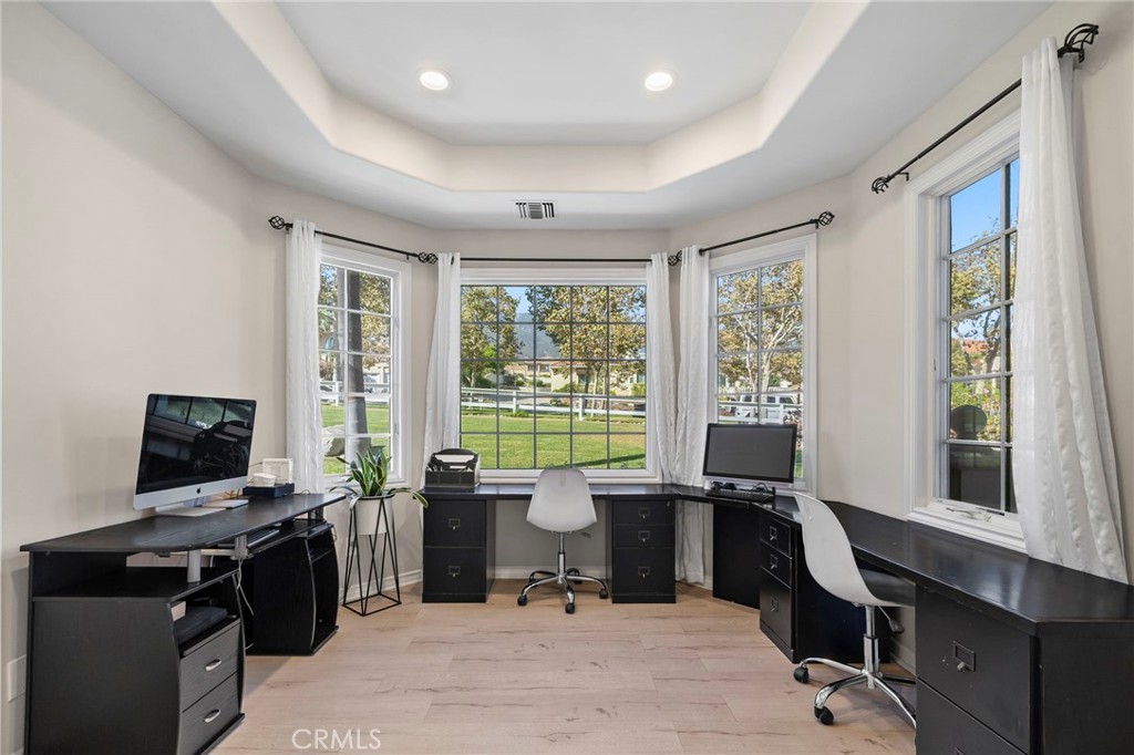 Home office with black built-in desks, white chairs, and large windows overlooking a green lawn.