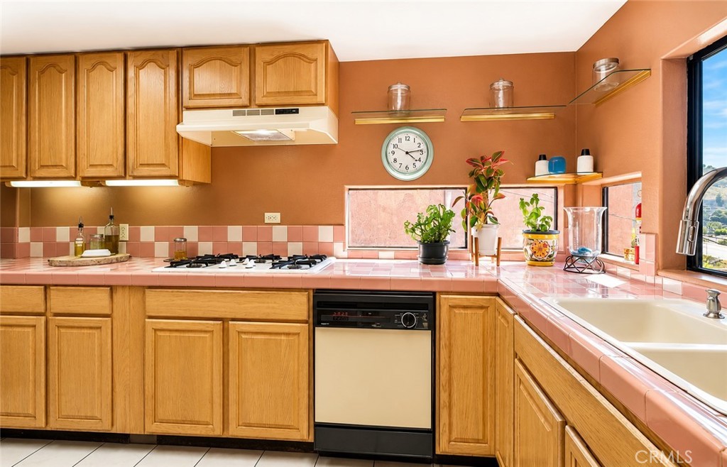 Kitchen with wood cabinets, pink tile counters, a gas cooktop, and a sink beneath a window.