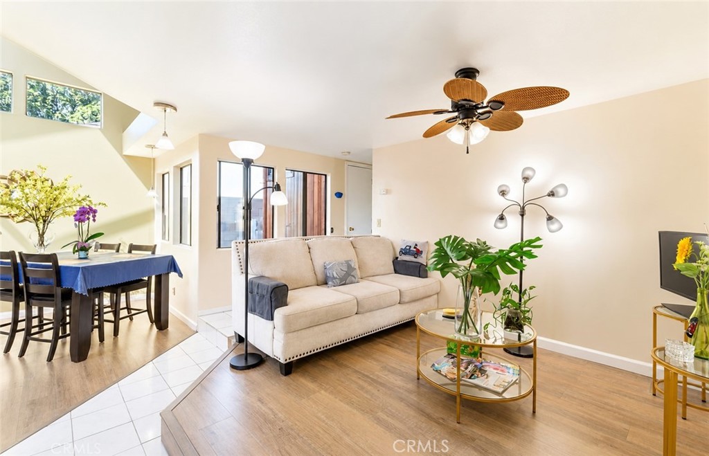 Open living and dining area with a beige sofa, glass coffee table, and ceiling fan.