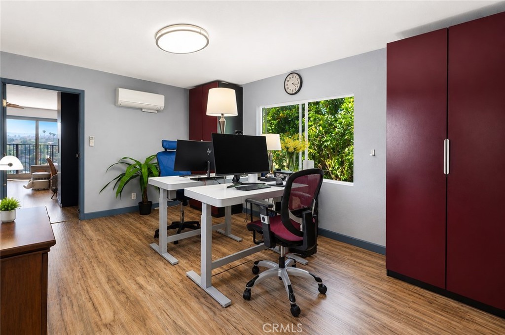 Furnished home office with dual desks and burgundy cabinets beside a window overlooking greenery.