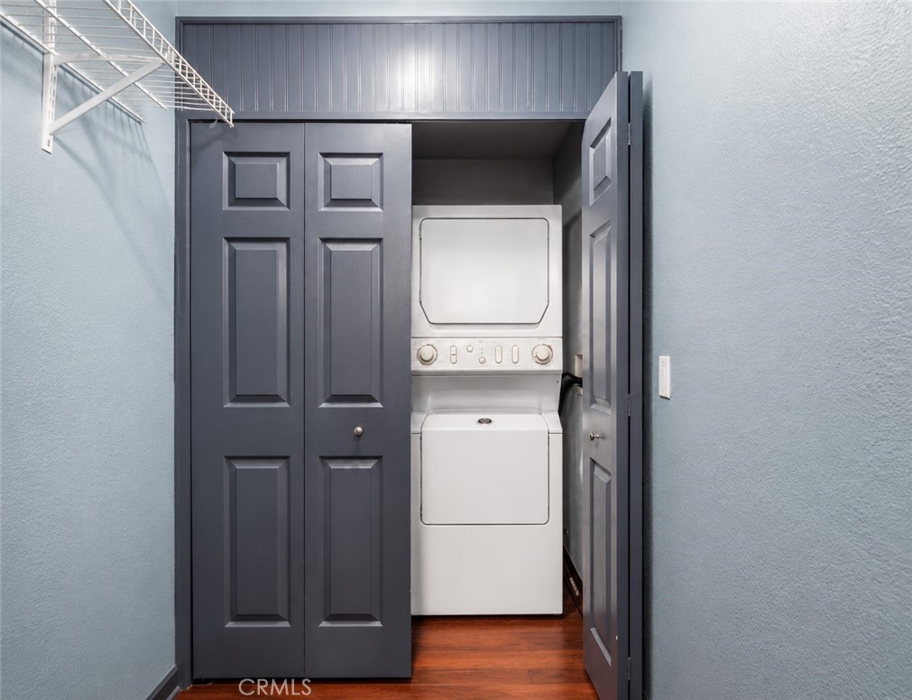 Laundry closet with a stacked washer and dryer behind open dark paneled doors.
