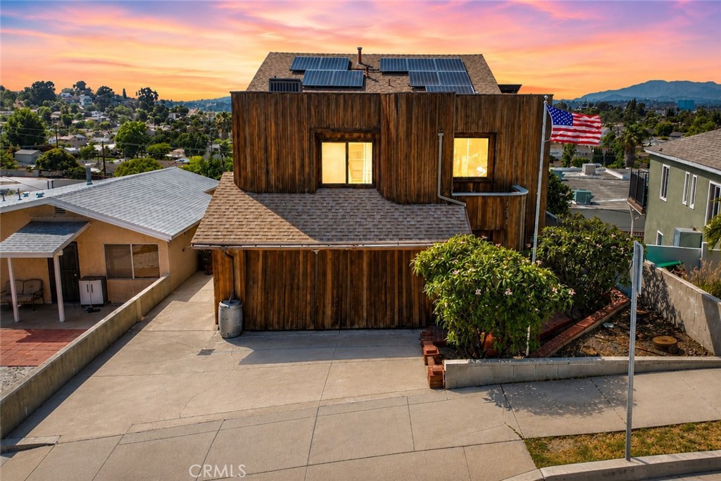 Wood-sided home with rooftop solar panels and a broad concrete driveway at sunset.