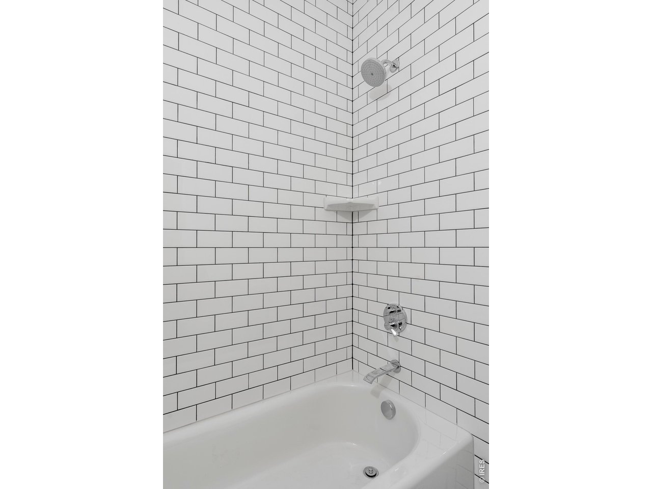 Bathroom with a white bathtub and shower, chrome fixtures, and white subway tile.